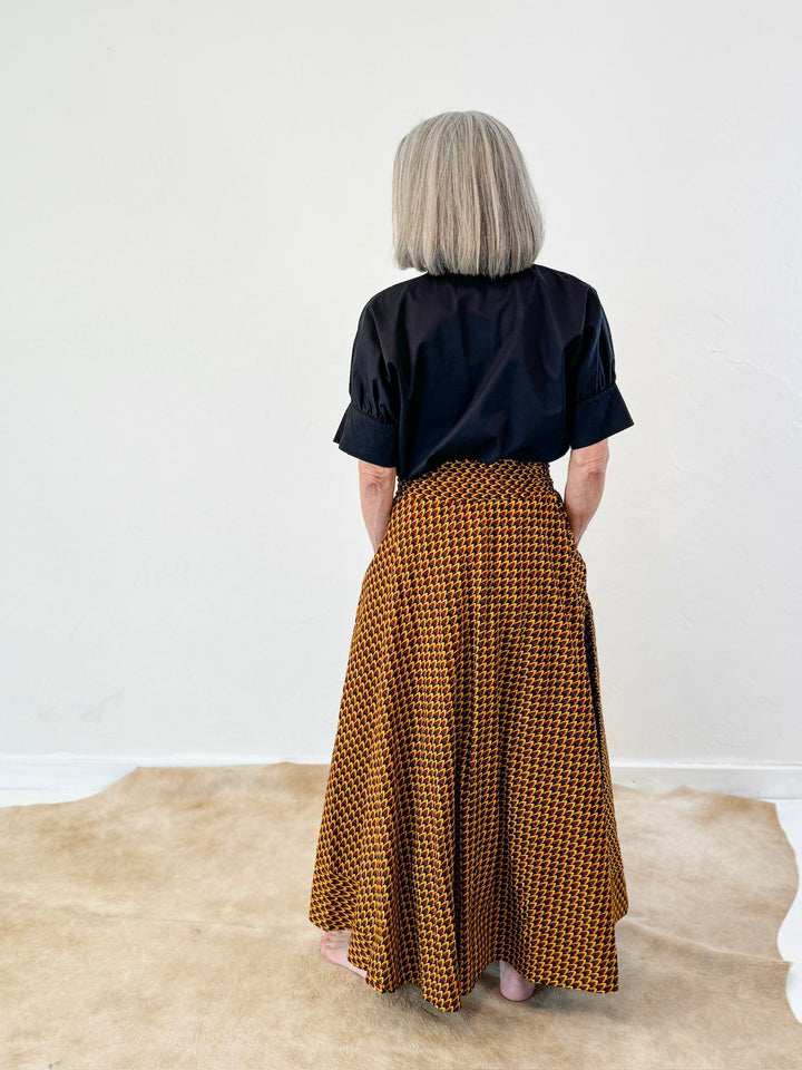 Model is wearing a bold yellow skirt with small scale design with red and black. Model has paired it with short sleeve black ruffle collar shirt by Heidi Houston. Front view.