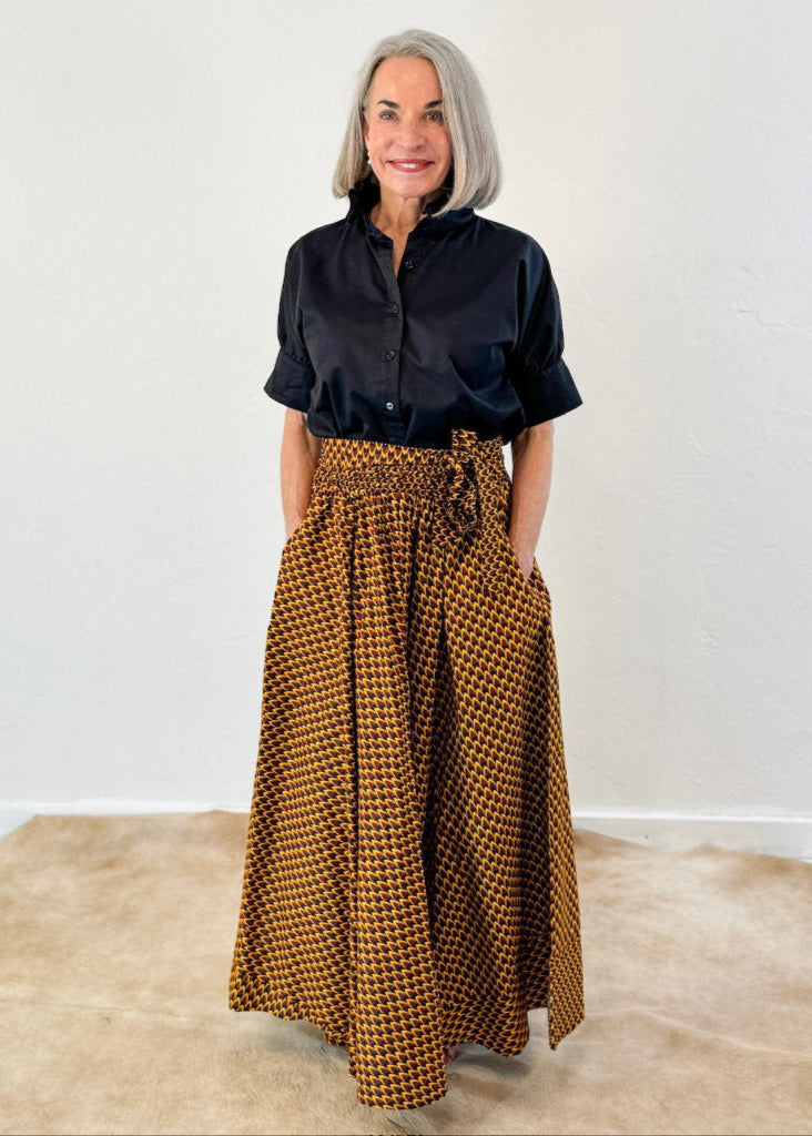 Model is wearing a bold yellow skirt with small scale design with red and black. Model has paired it with short sleeve black ruffle collar shirt by Heidi Houston. Front view.