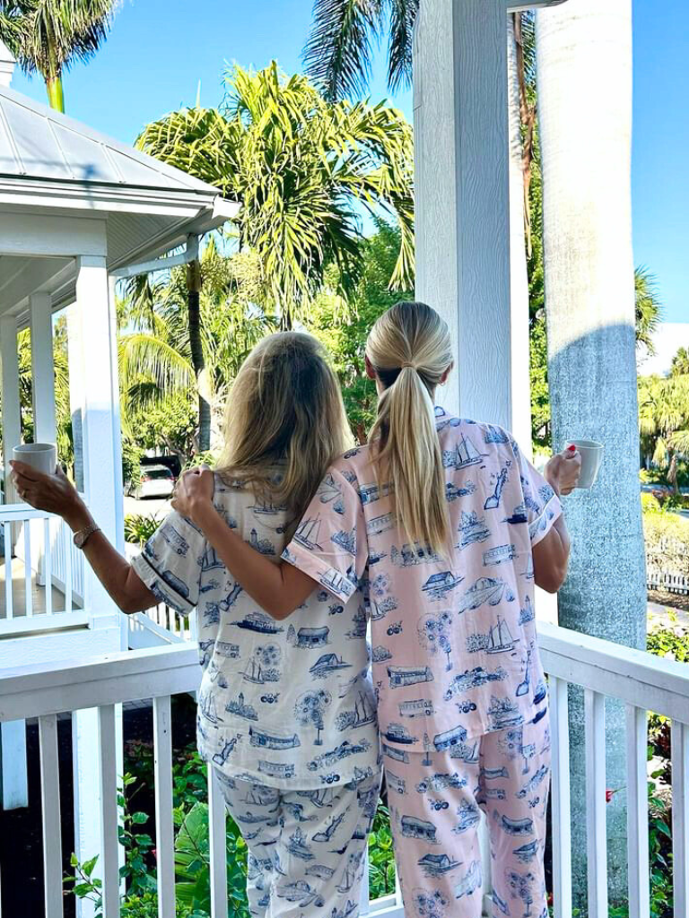 Mother and adult daughter standing on the porch enjoying a cup of coffee in their Door County pajamas in both navy & white and pink & navy.