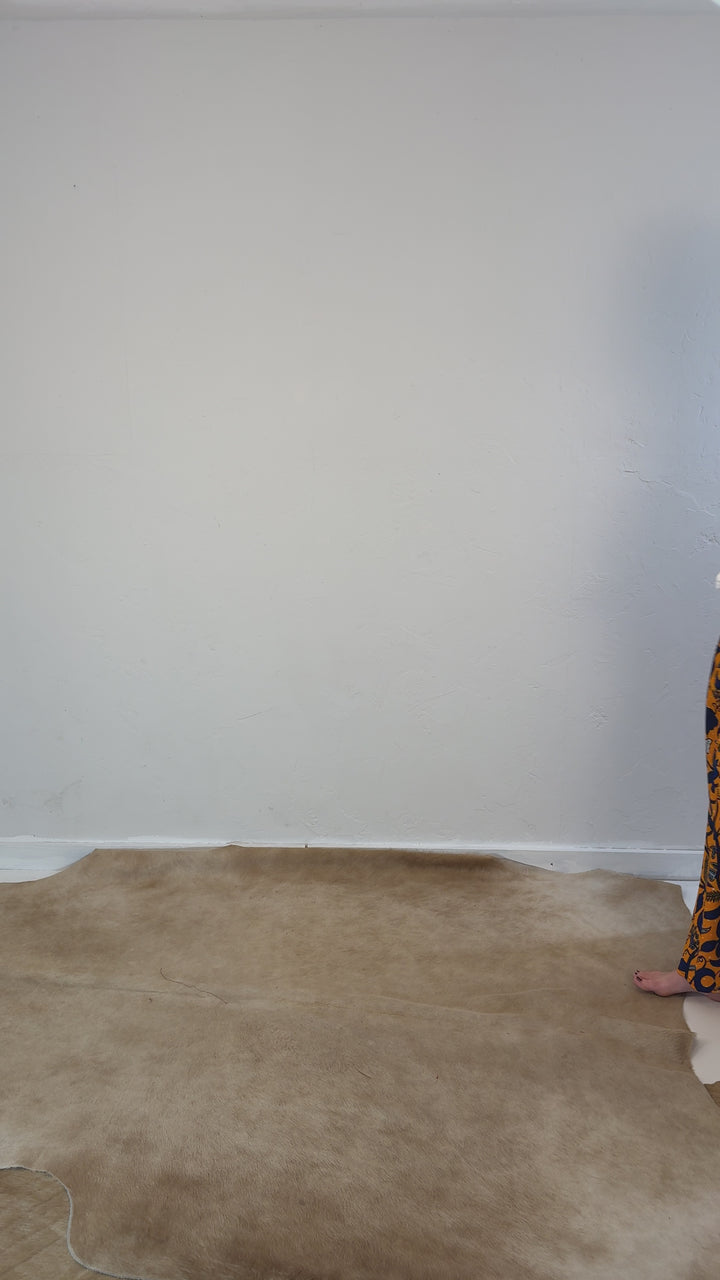 Model walking into frame wearing an orange maxi skirt with bold floral pattern in dark blue. Model has paired with a long sleeve white ruffle collar shirt by Heidi Houston. 